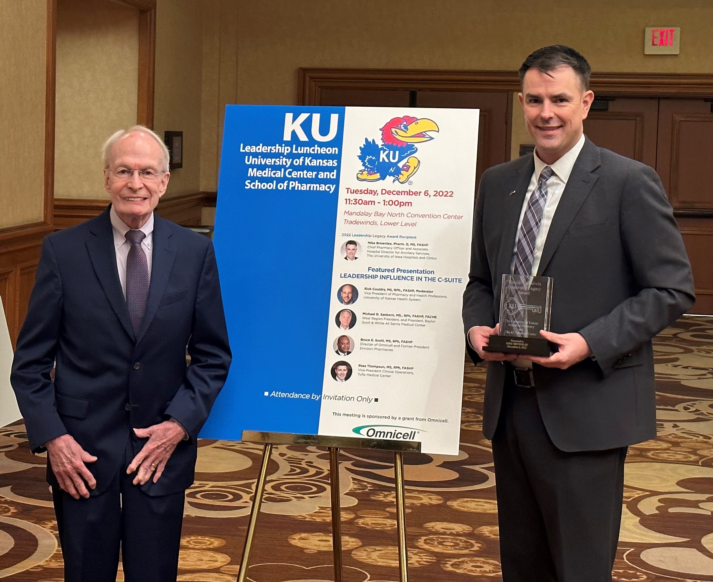 Harold Godwin and Mike Brownlee stand in front of a poster recognizing Brownlee as the 2022 Harold N. Godwin Leadership Legacy Award recipient.