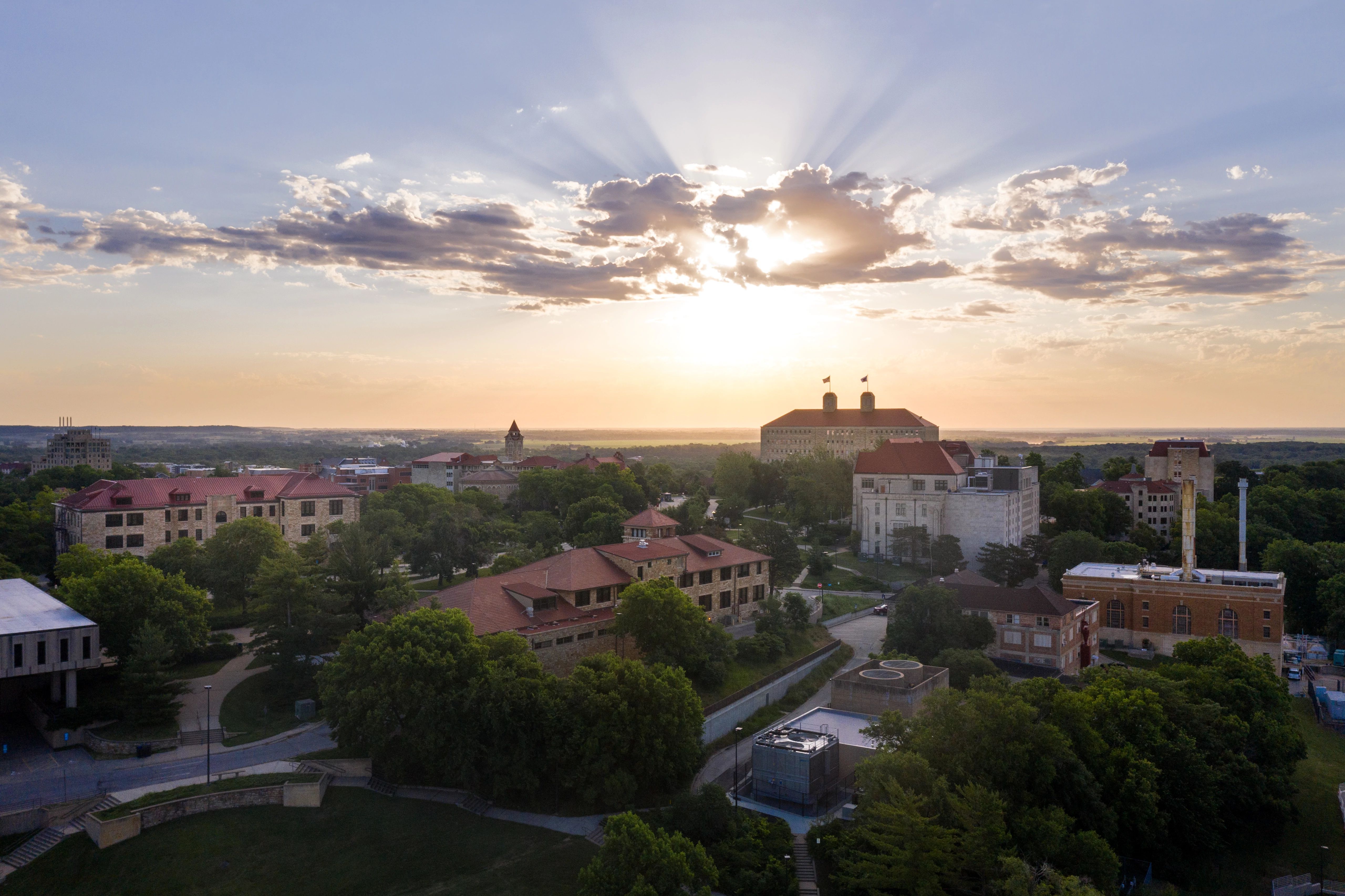 An aerial image of the University of Kansas Lawrence campus with the sun rising in the background.