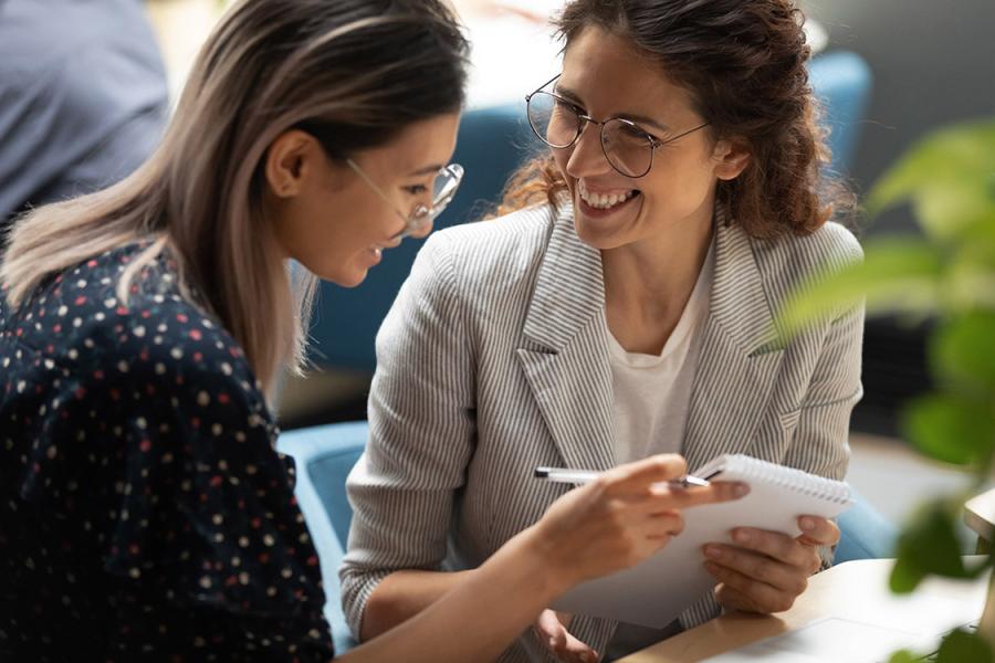 Two women comparing notes in a notebook and smiling.