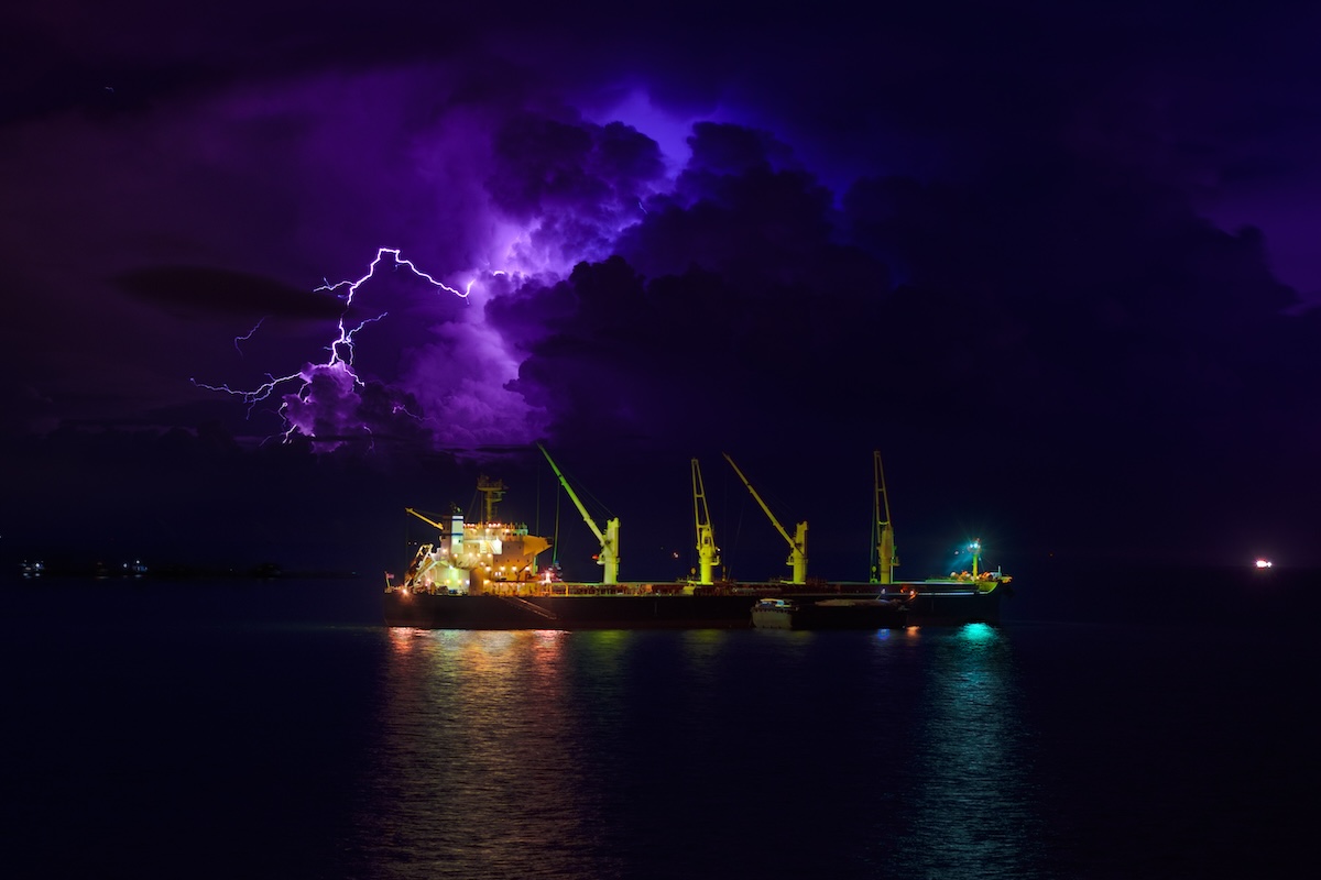 A photo of an industrial ship with lightning overhead.