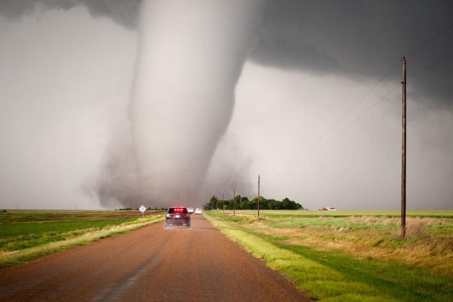 Car driving toward tornado in rural Kansas area.