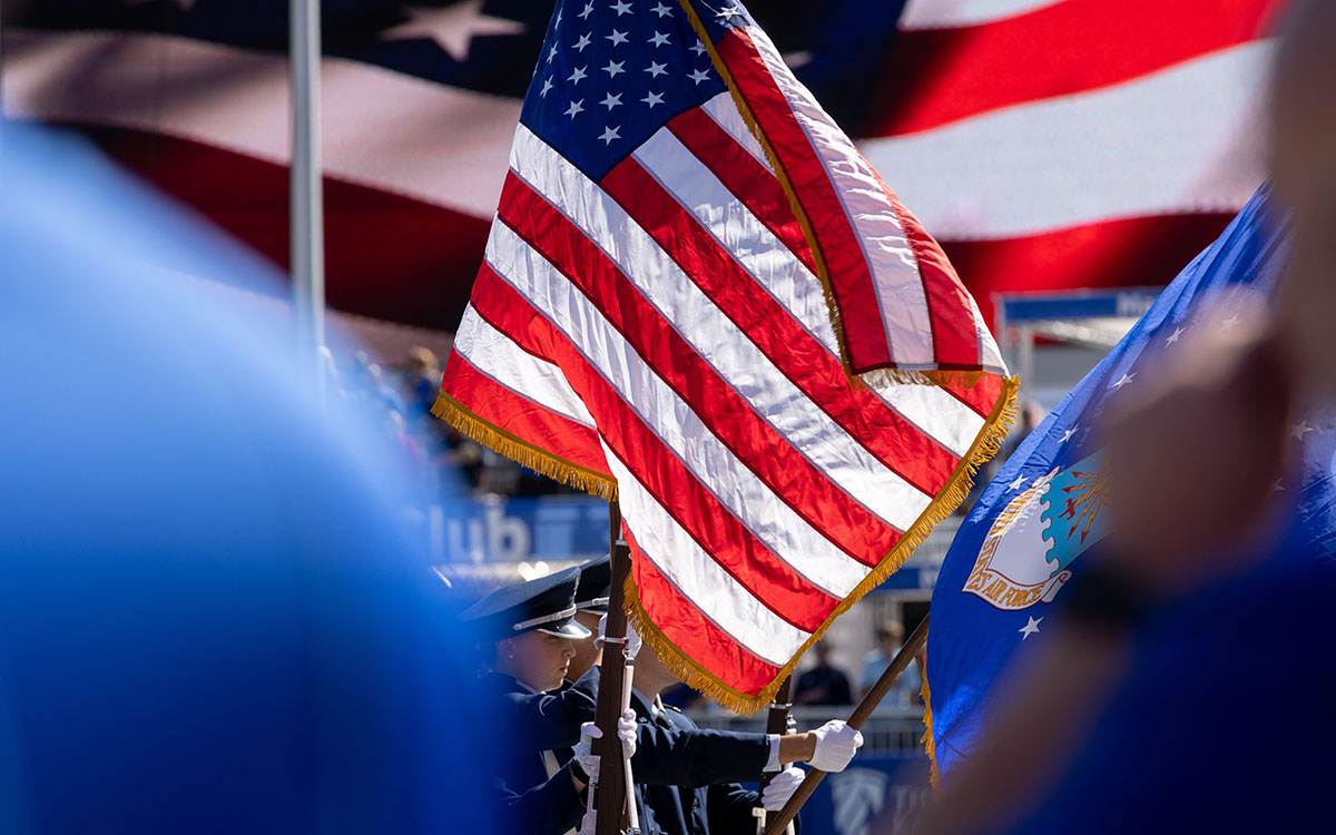 KU ROTC members carry American flag at sporting event.