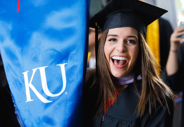 graduate smiling, holding up KU banner