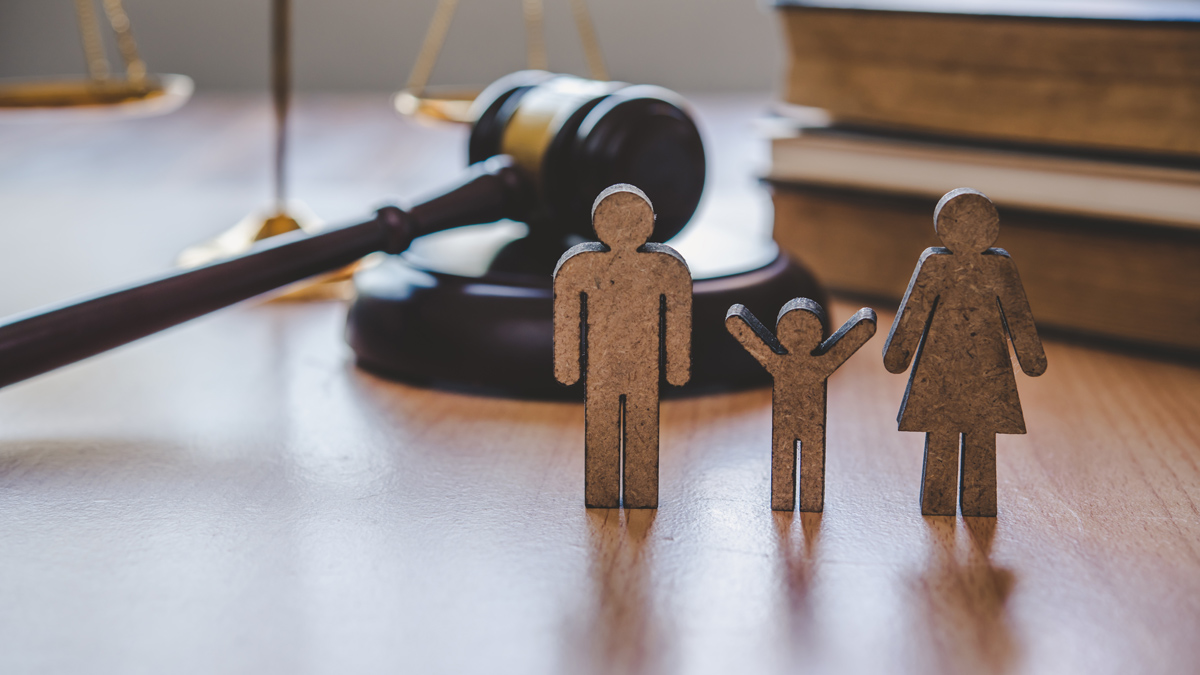 Photo illustration of wooden family figures in front of law books and a gavel