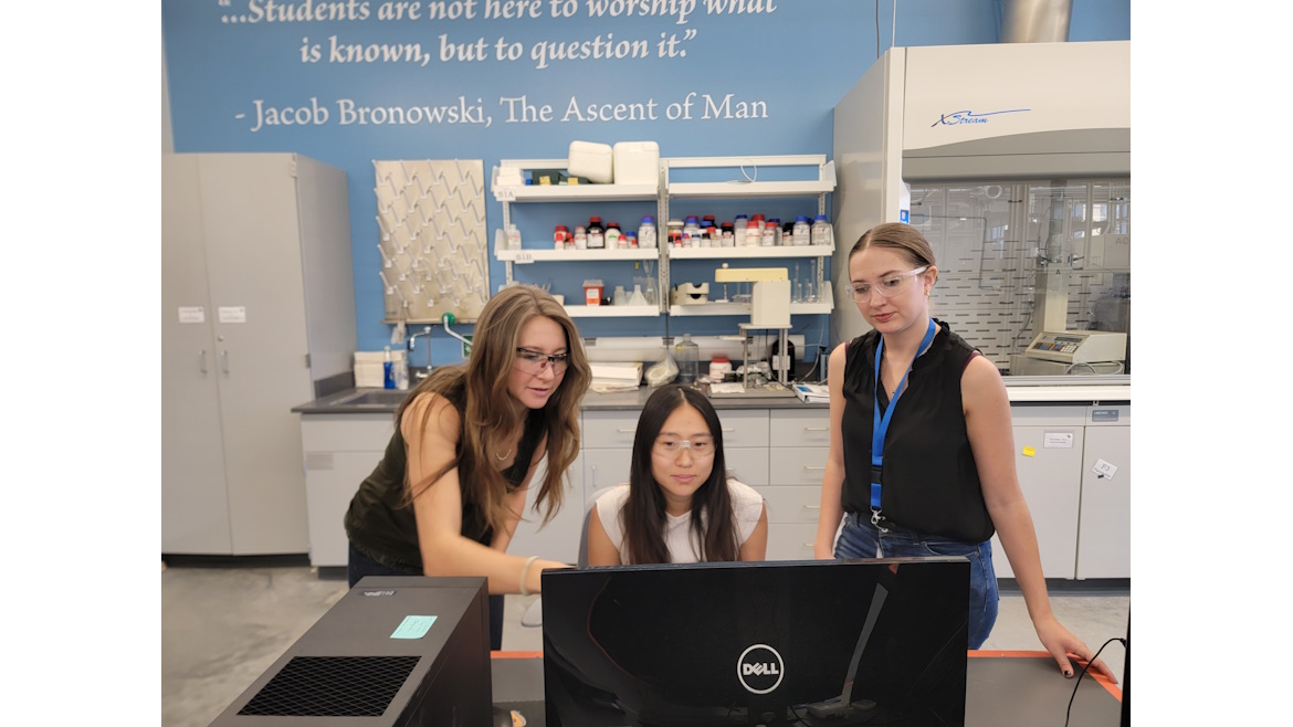 Three women in the lab with goggles on looking at data on a computer
