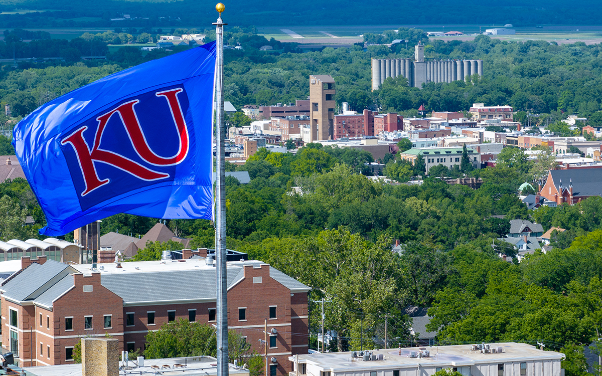KU flag flying on rooftop with view of downtown, north Lawrence in distance.