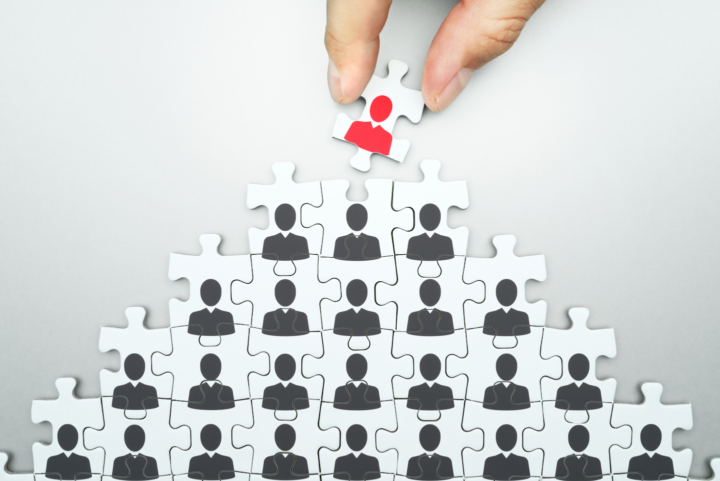 Stock image of pyramid of puzzle pieces with corporate figures on each piece.