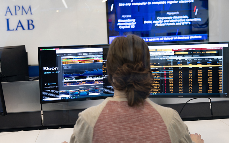 A girl sits in front two computer monitors while navigating the Bloomberg Terminal.