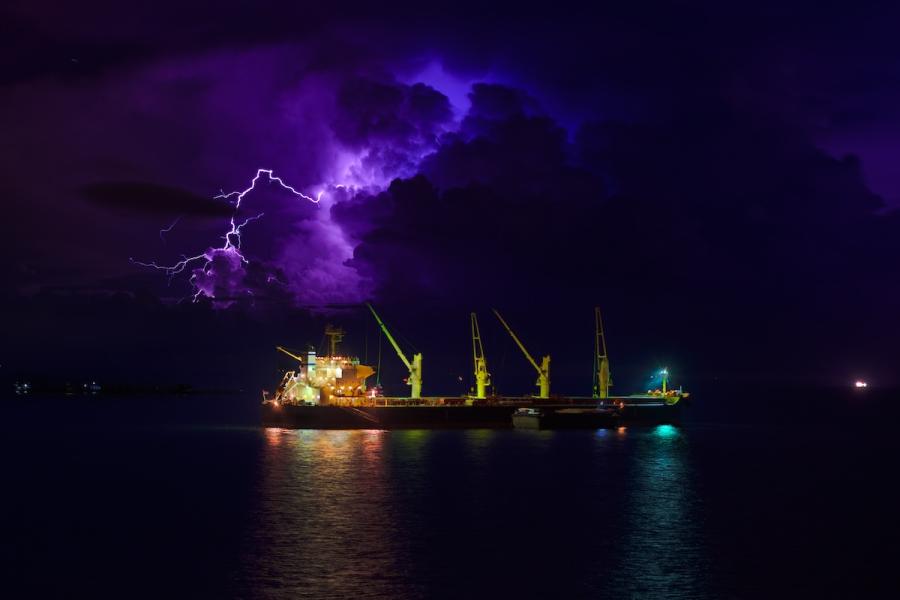 A photo of an industrial ship with lightning overhead.