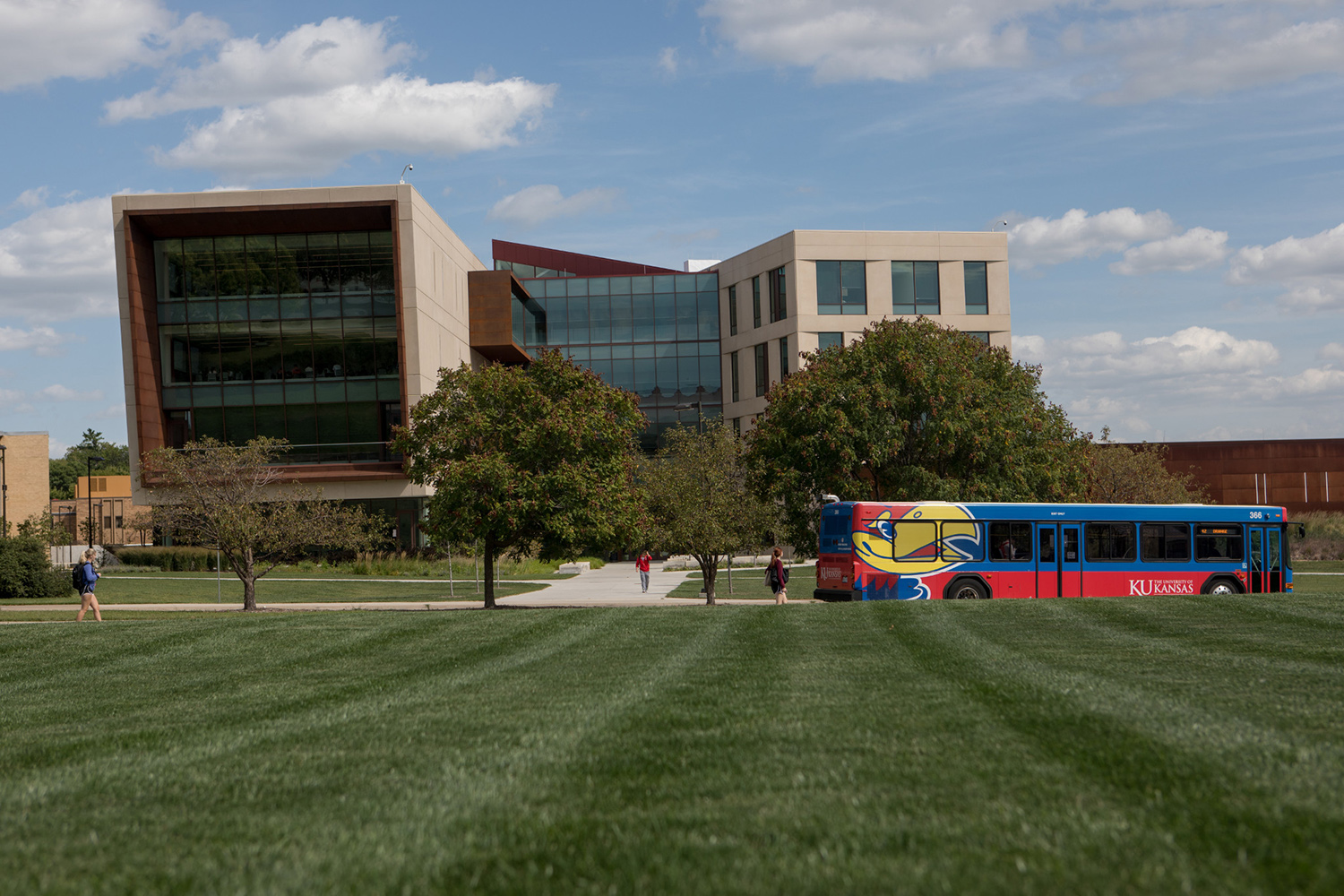The west-facing exterior of Capitol Federal Hall with a KU bus driving by on Naismith Drive.