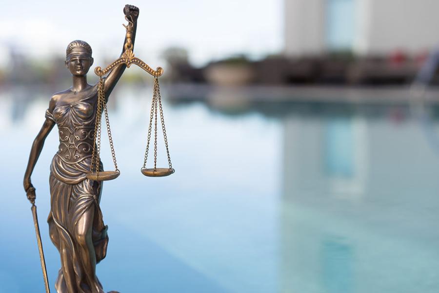 A photo illustration of the blind justice statue near water.