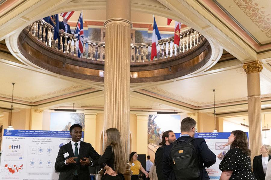 View of students in professional attire with research posters. Above are flags encircling the Capitol rotunda overlooking the presentation area.