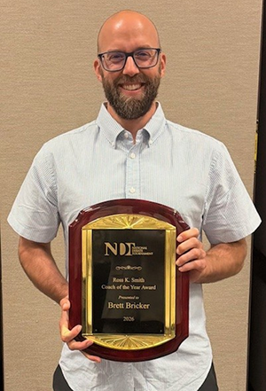 Brett Bricker holding plaque for the top coaching award at the 2026 National Debate Tournament.