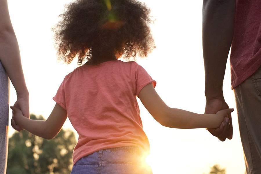 An image of parents holding hands with a child as the sun sets in the background of the happy family.