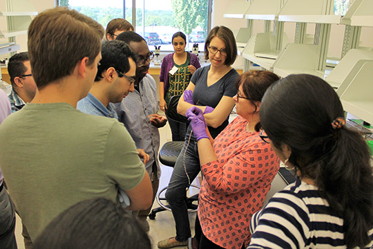 Maggie explains to the group how the high impedance current source supplies current through the two outer probes on the chip, and a voltmeter measures voltage across the inner two probes to determine sample resistivity.