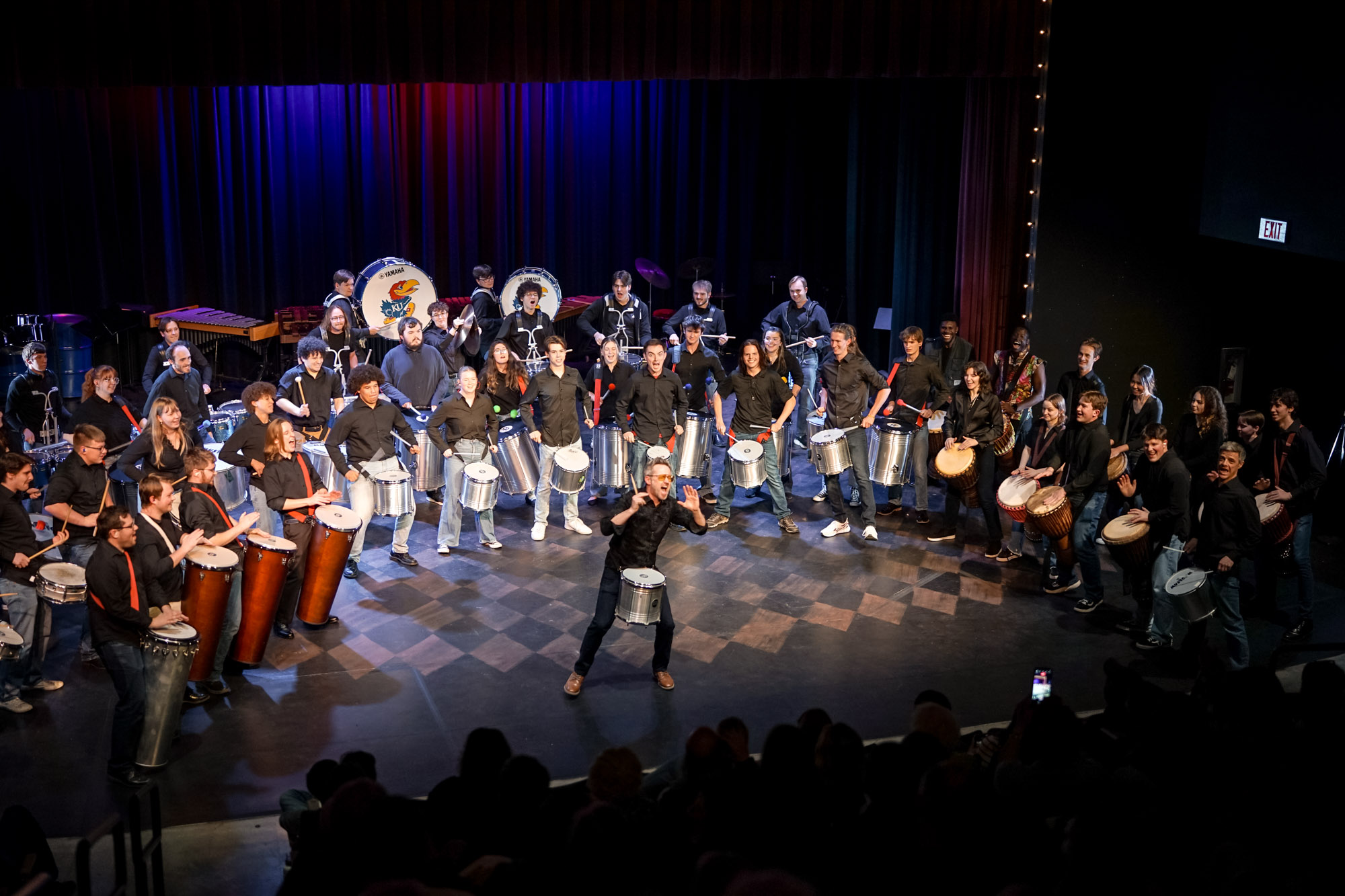 A large group of people holding various percussion instruments onstage.