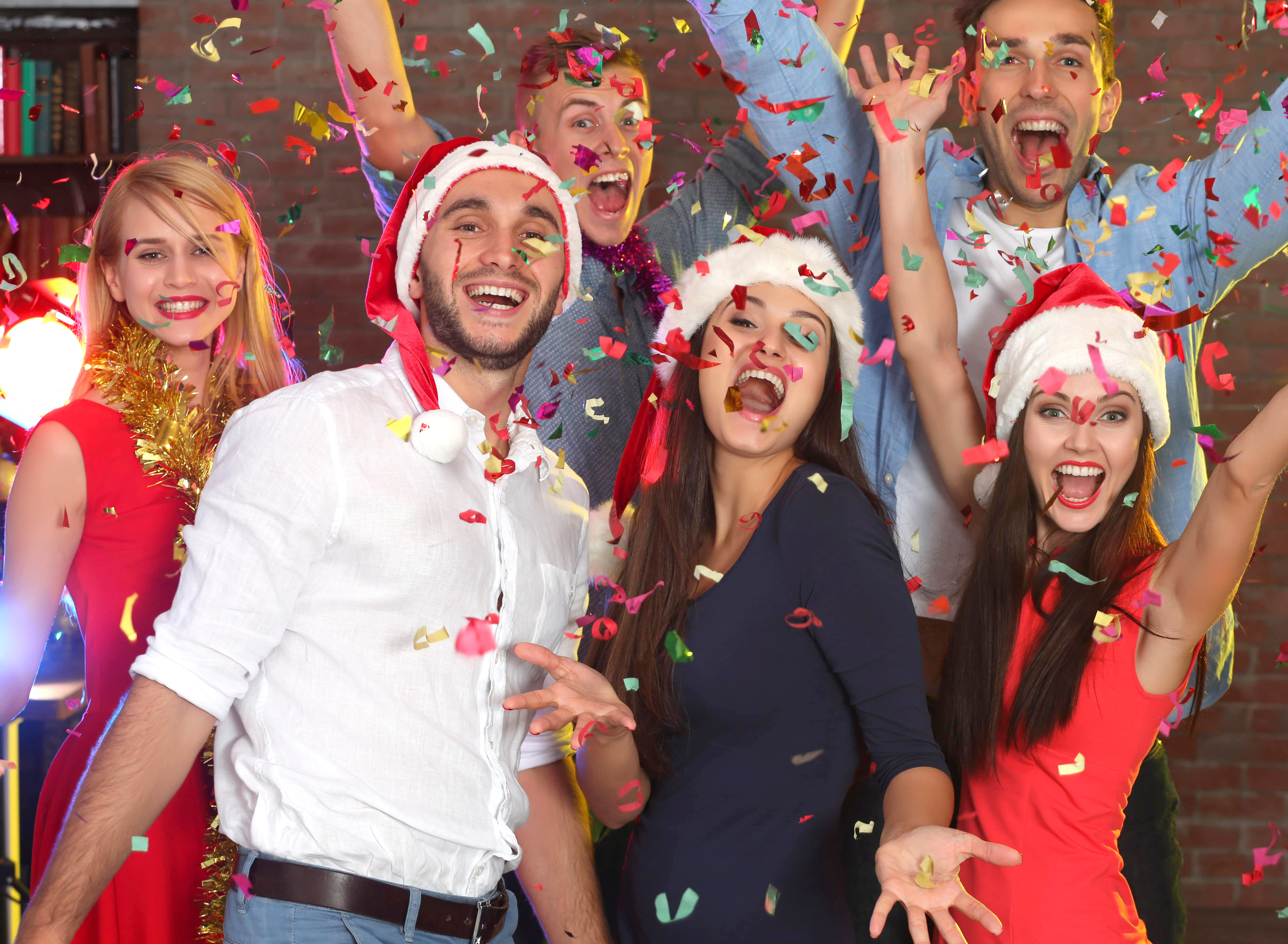 A group of people celebrate and throw confetti while wearing Santa hats.
