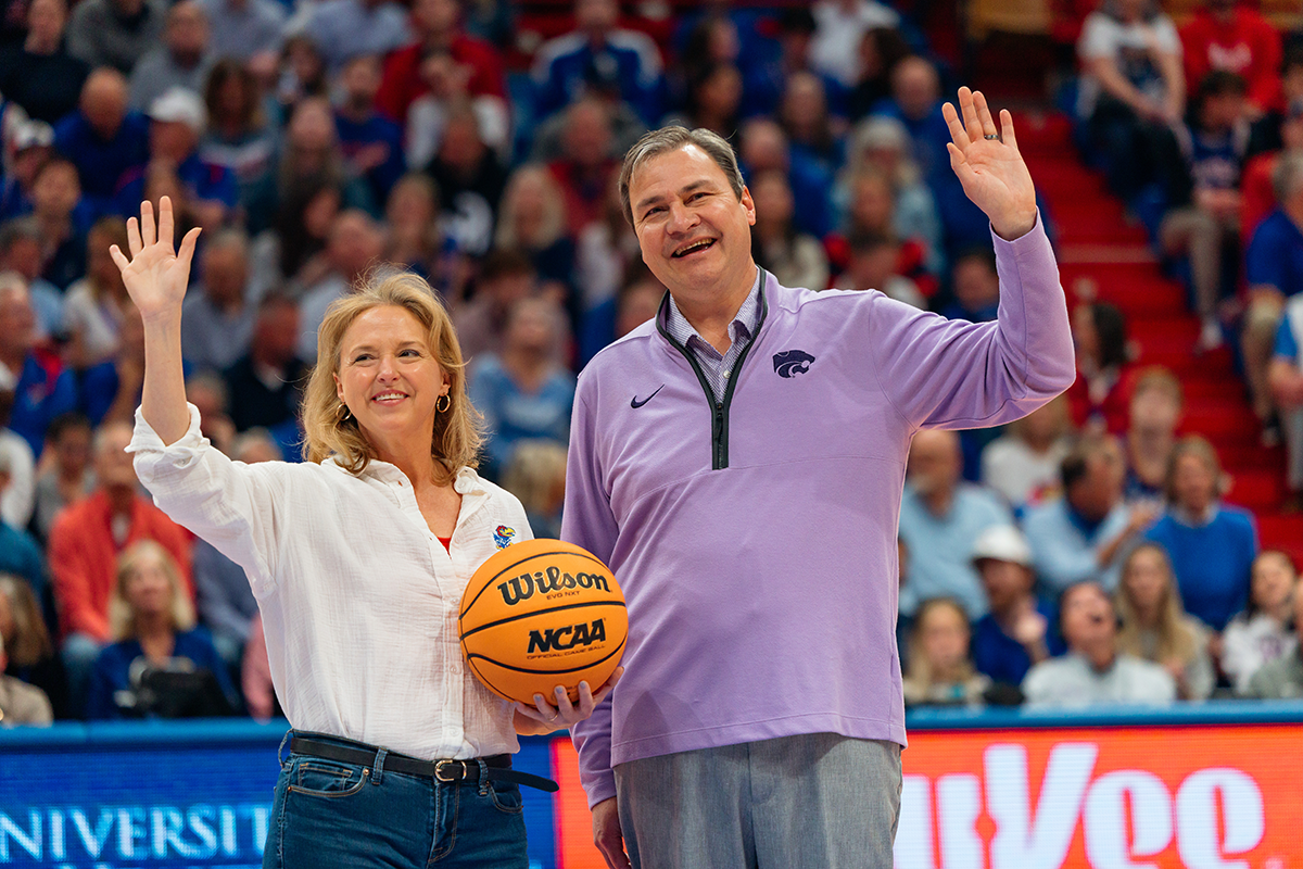 Shelley Hooks, vice chancellor for research at the University of Kansas, and Hans Coetzee, vice president for research at Kansas State University, hold a basketball and wave to the crowd from center court at KU's Allen Fieldhouse during a timeout at the KU vs. K-State men's basketball game on March 7, 2026.