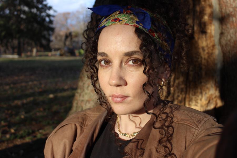 Woman with brown eyes and curly hair sitting in front of a tree