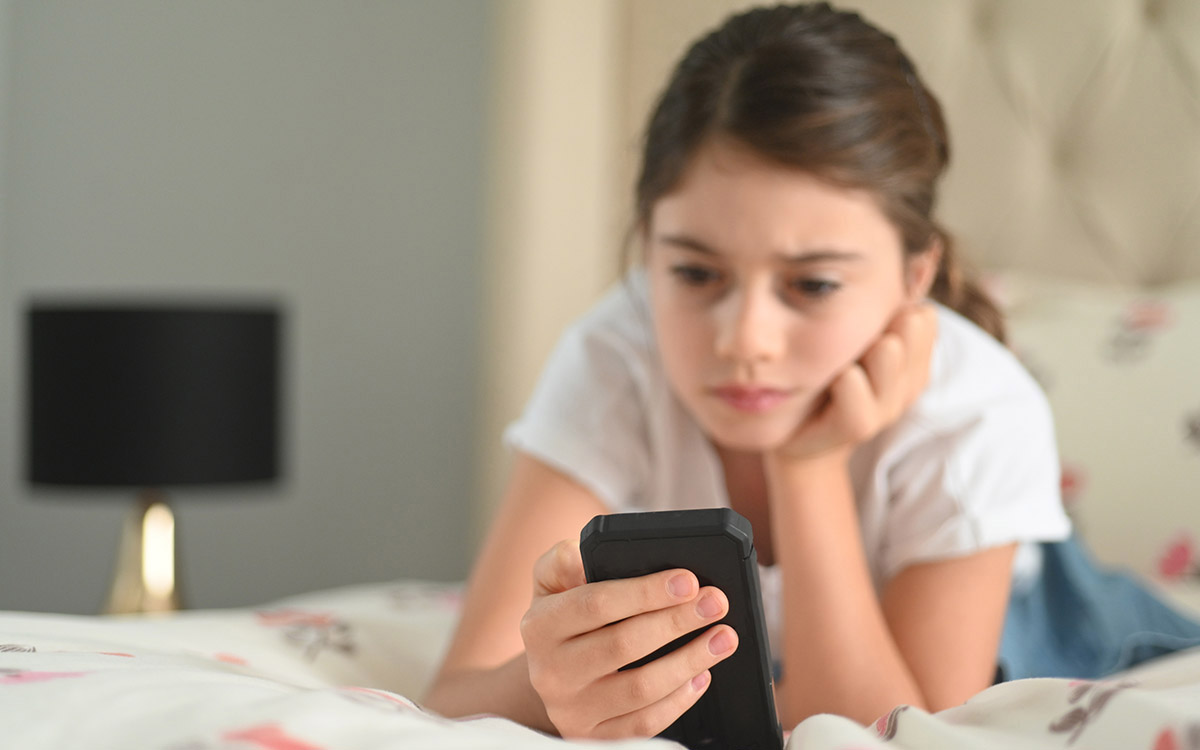 Girl laying on bed looking at smartphone.