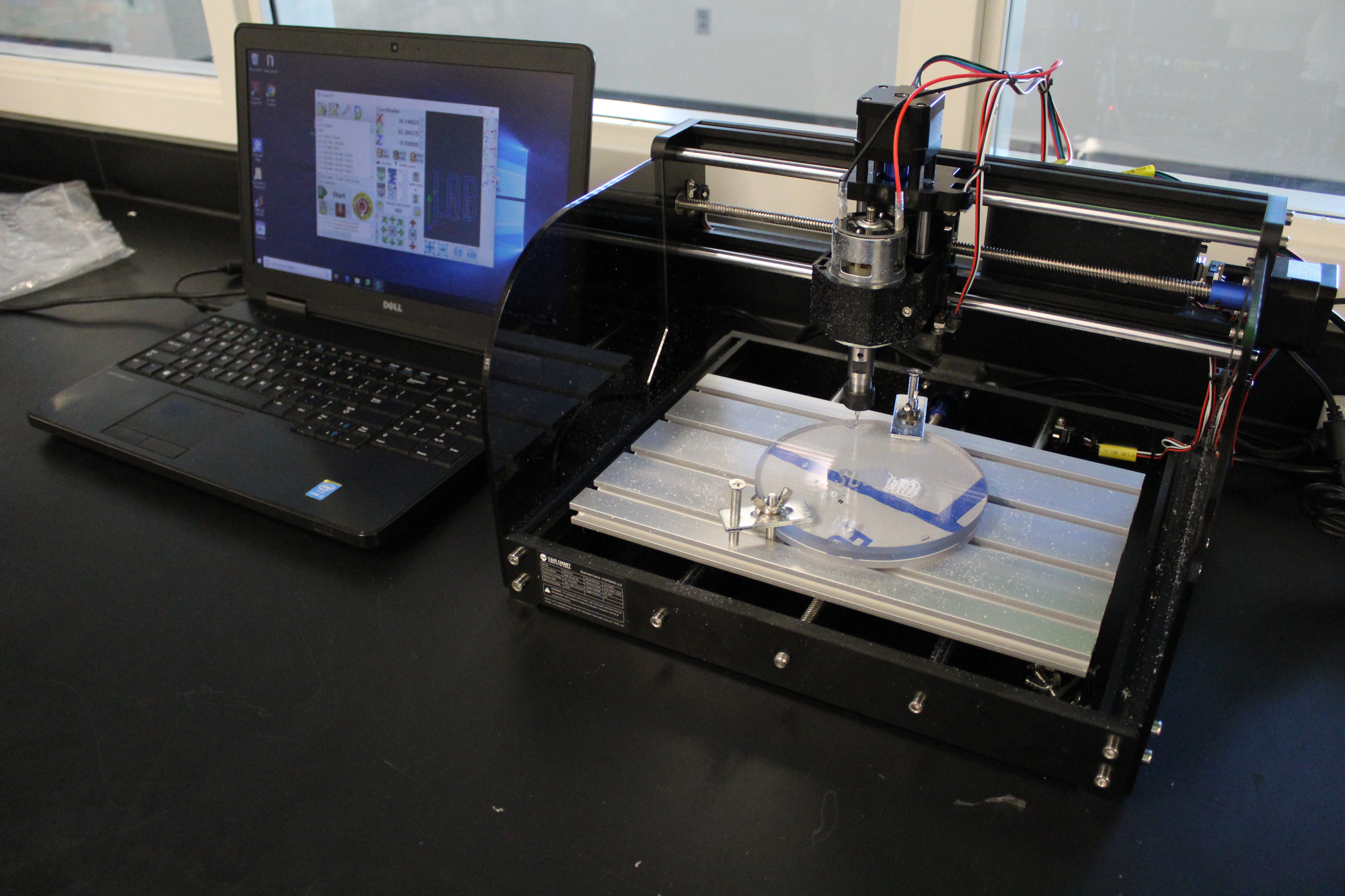 Computer placed on a black table adjacent to a machine actively working on a task.