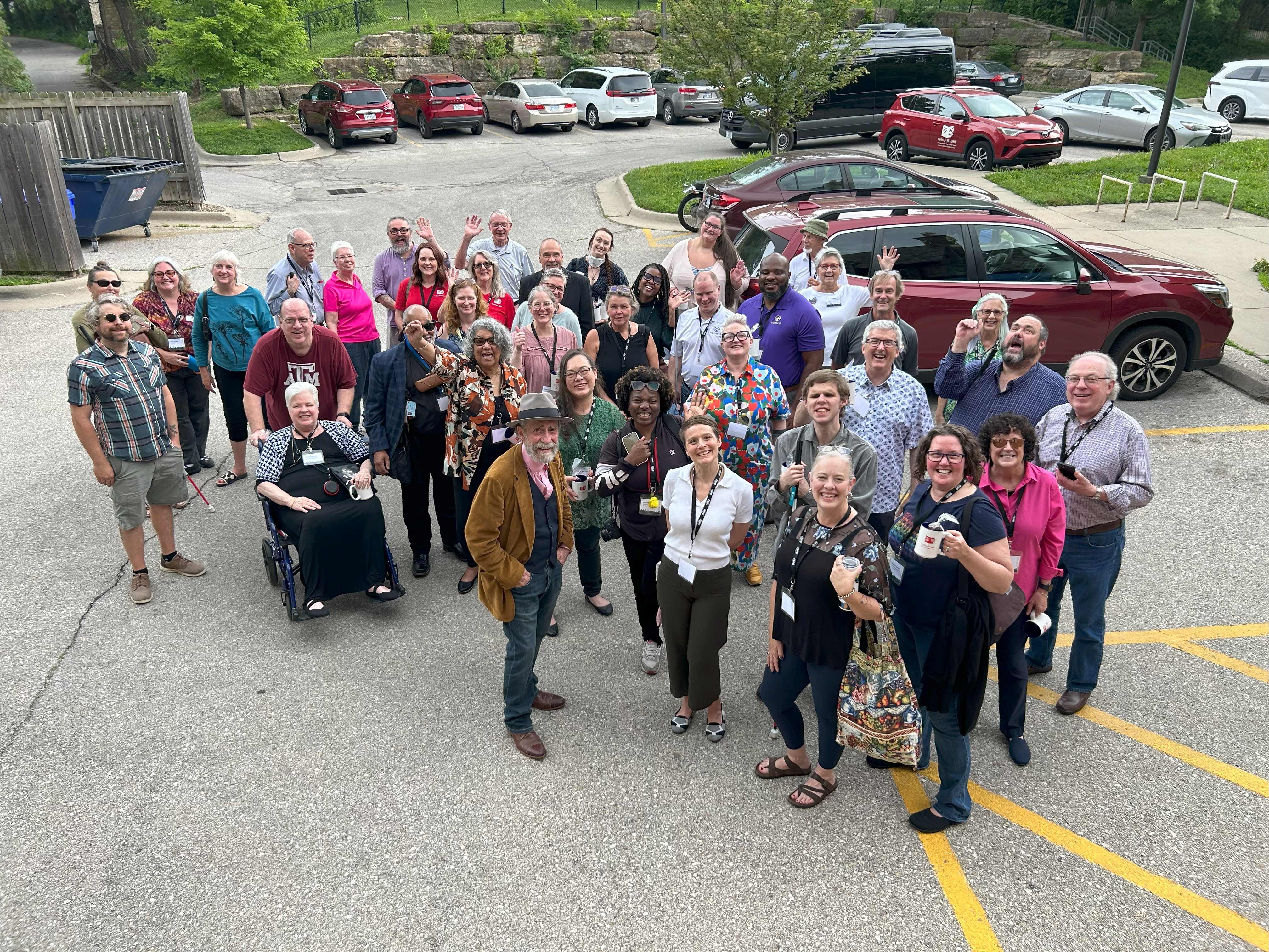 three dozen people stand in the Audio-Reader parking lot looking up at the camera aimed down at the crown from a second story window. on a slightly cloudy day.