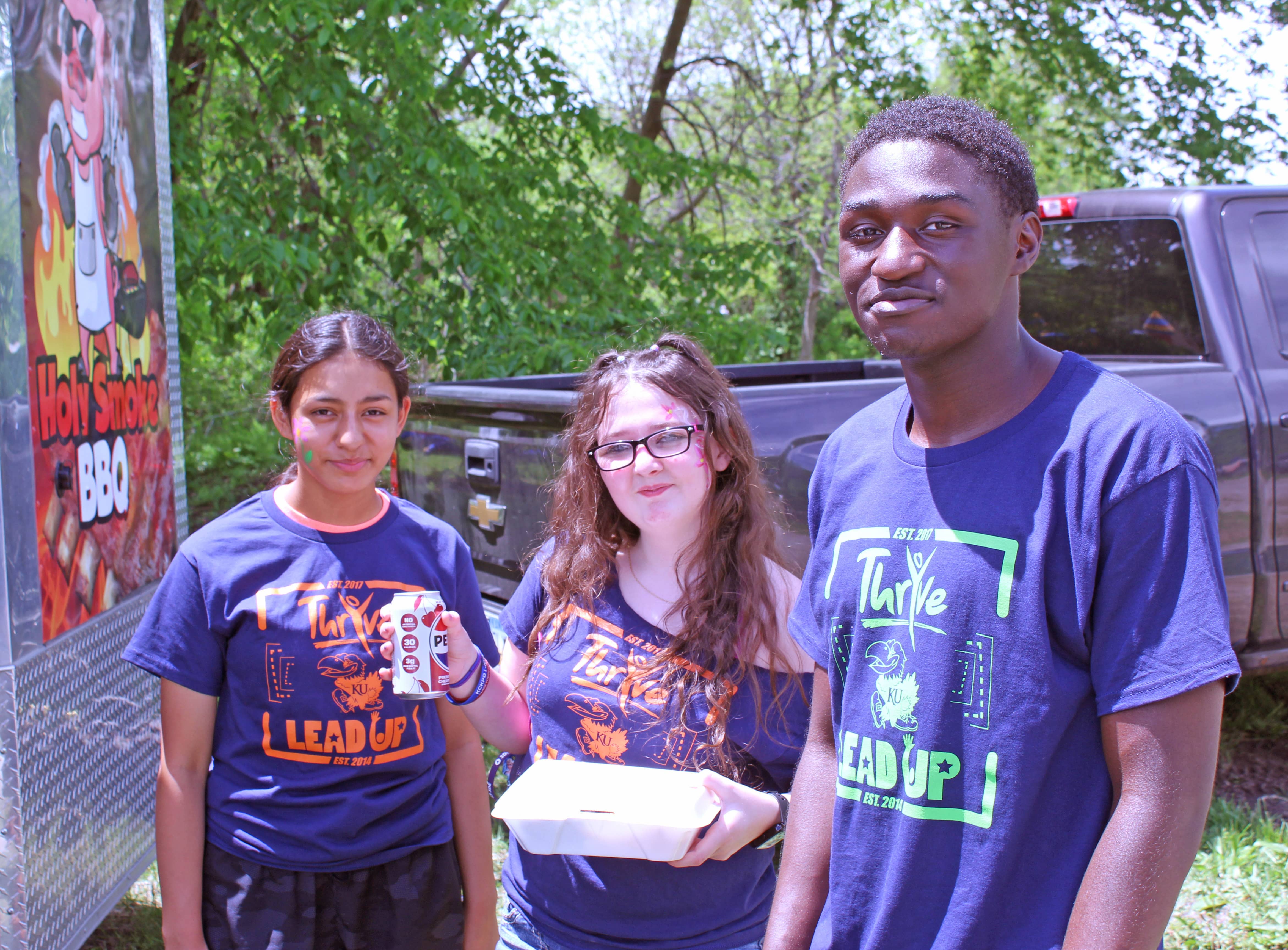 Three teenagers stand outside of a food truck at a community event.