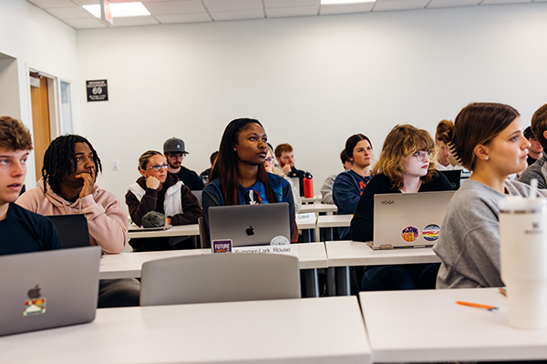 A group of students in a classroom look toward the front of the classroom.