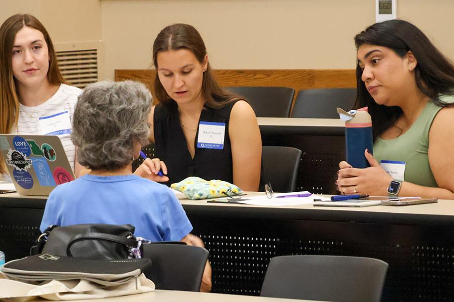 A group of law students seated with laptops converse with an attorney.