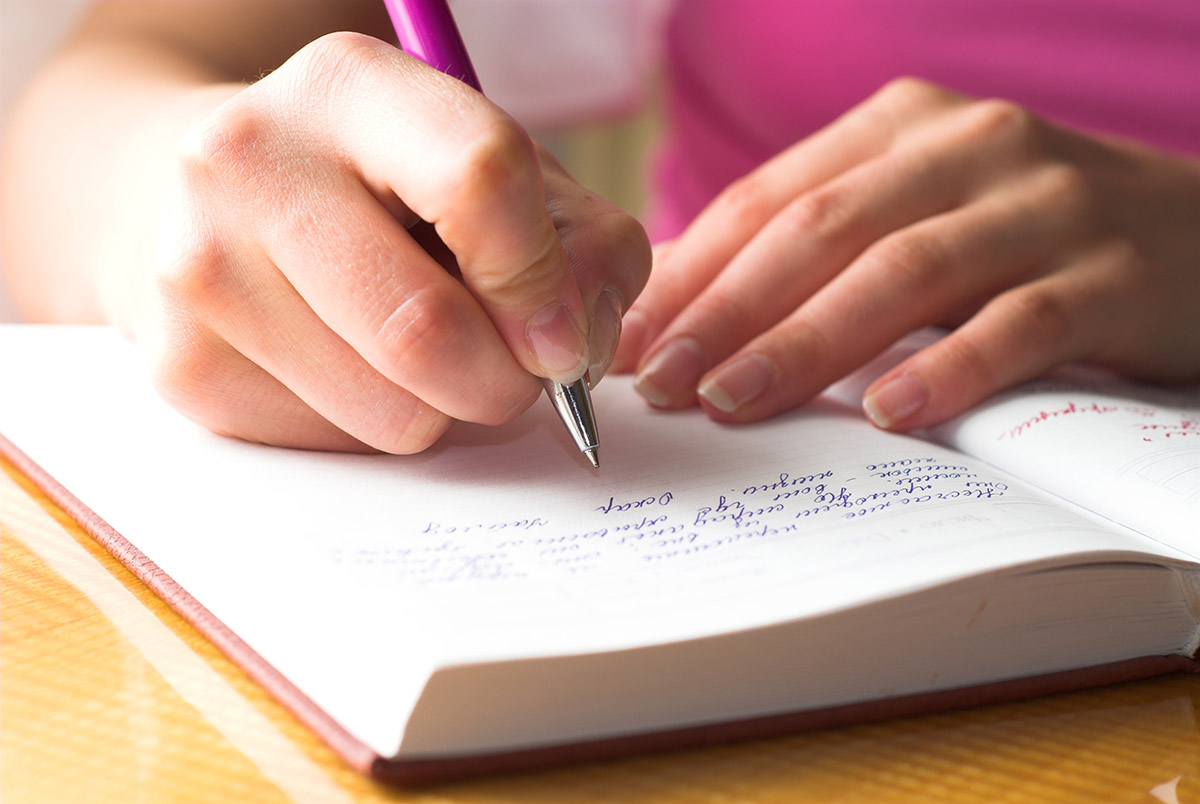 An image of a young person's hands, writing in a journal.