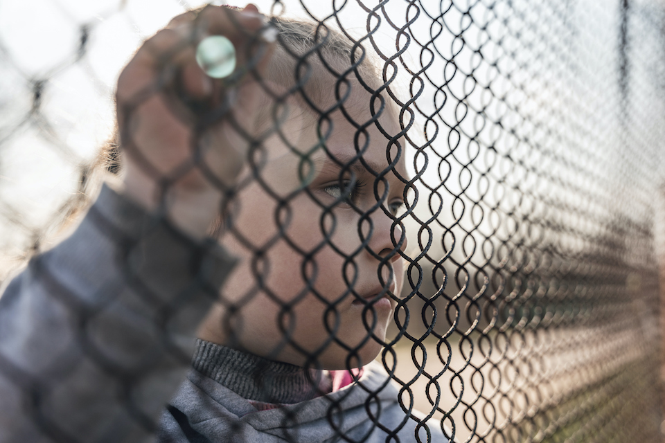 Child looking through fence links. IStock image.