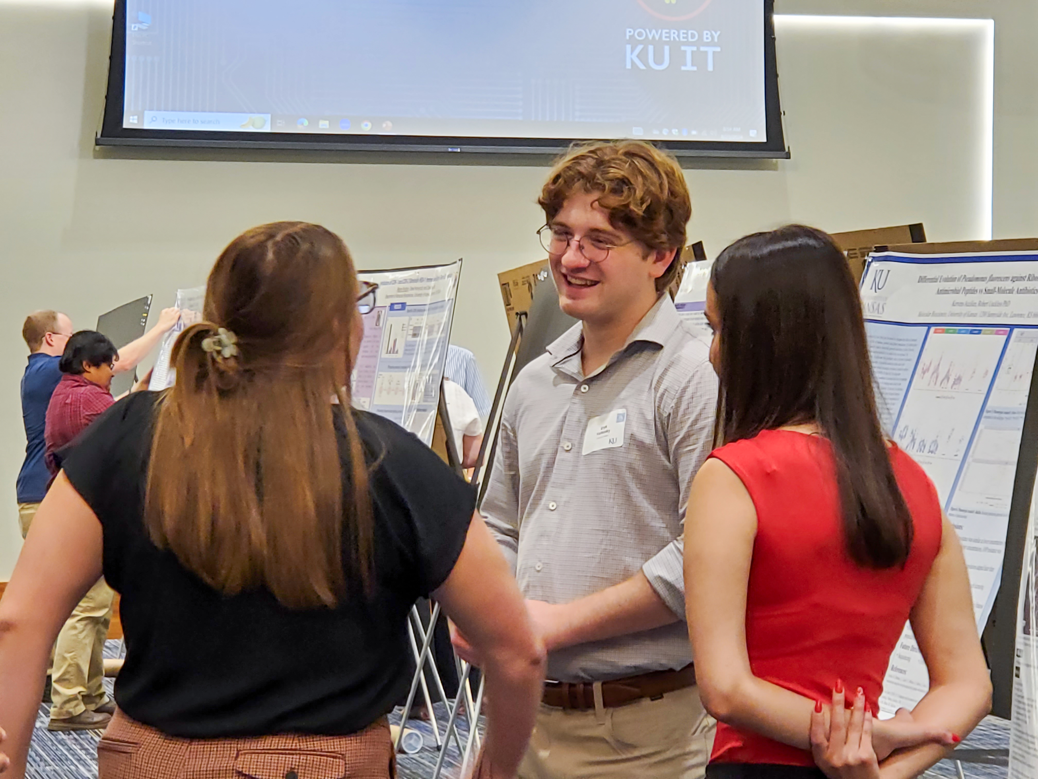 Graduate Student, Eryk Yarkowski speaking with two others infront of presentaion postesr