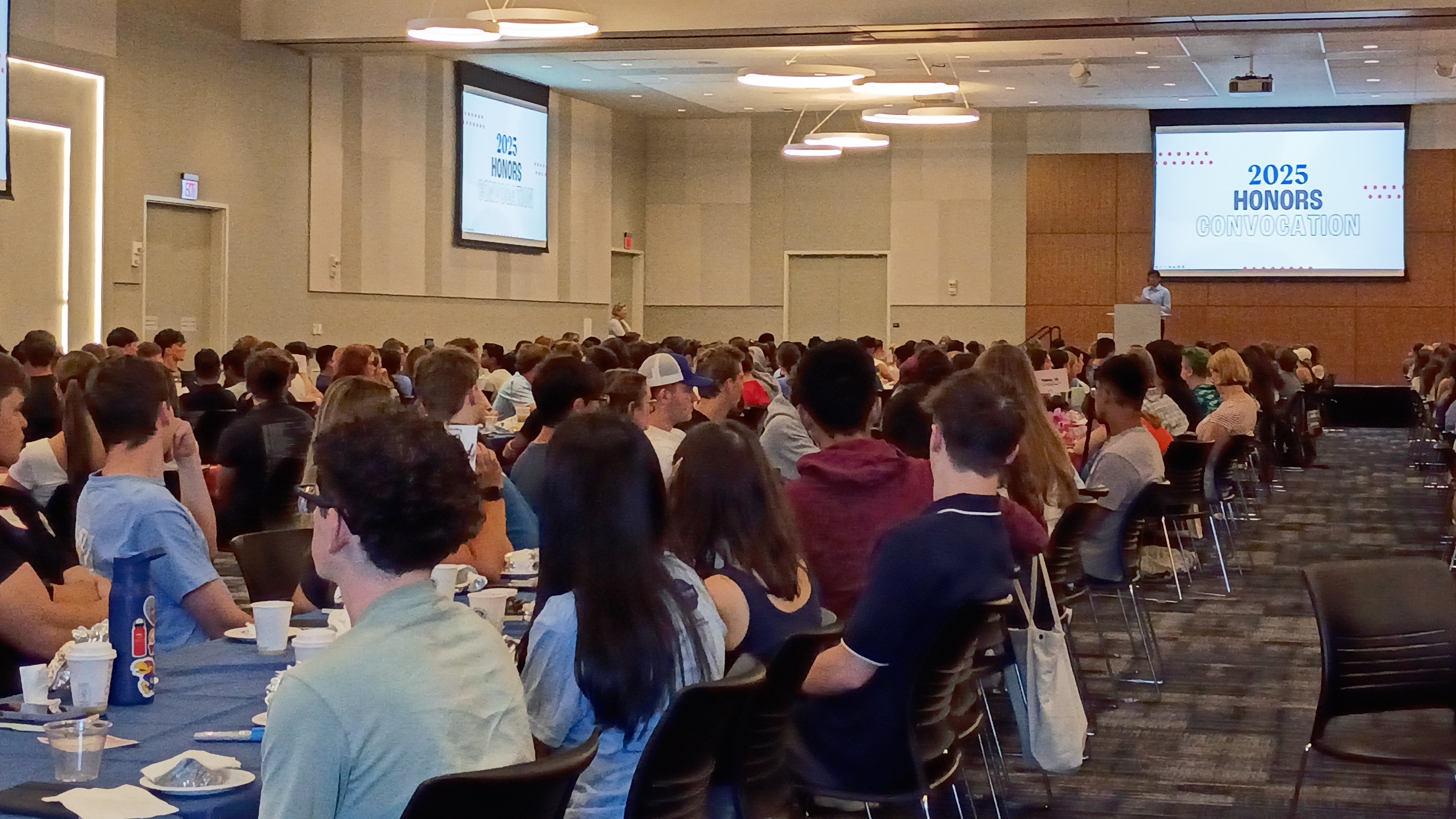 Student speaks from stage to a full ballroom of peers