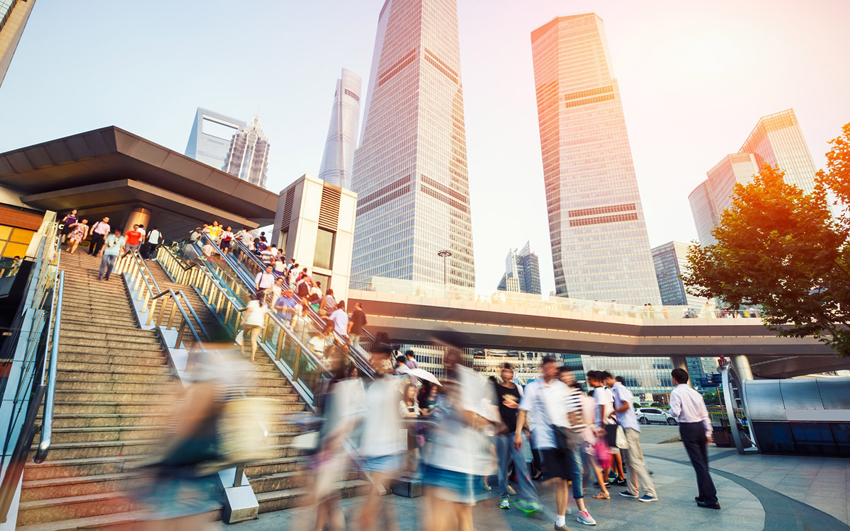 Individuals walk around downtown Shanghai with skyscrapers in background.