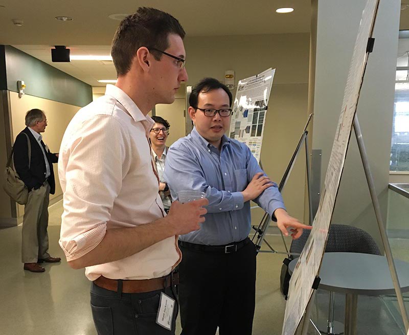 Two individuals engaged in discussion in front of a research poster.