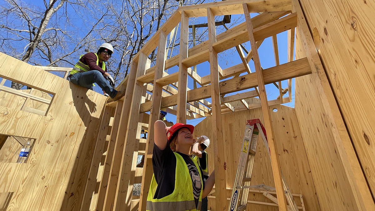 Two students work on wooden house frame for Phoenix House in Lawrence.