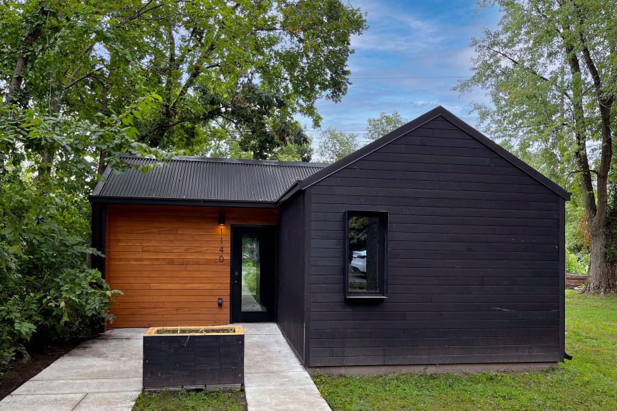 Exterior view of Phoenix House, a small modern house with clad in black and contrasting natural wood siding, surrounded by lush greenery.