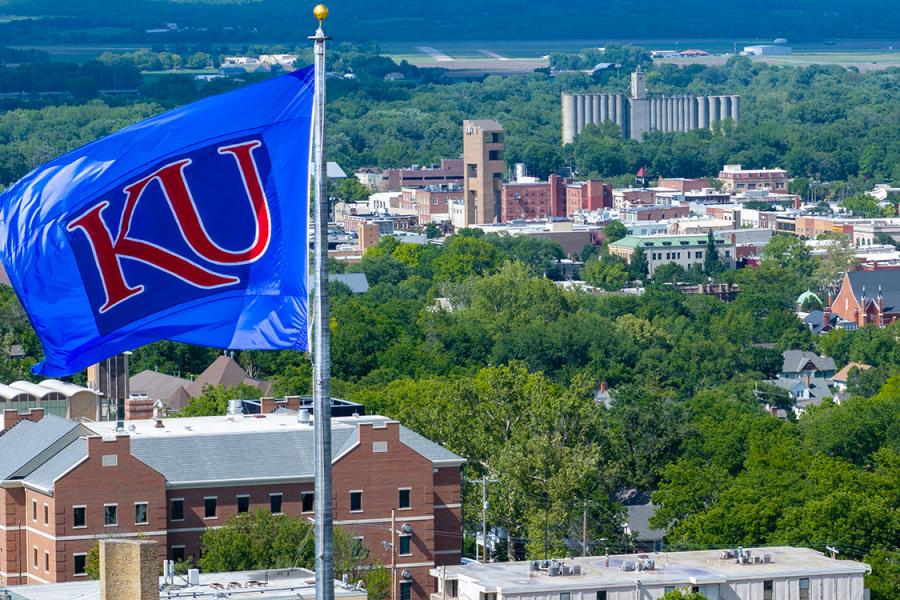 KU flag flying on rooftop with view of downtown, north Lawrence in distance.