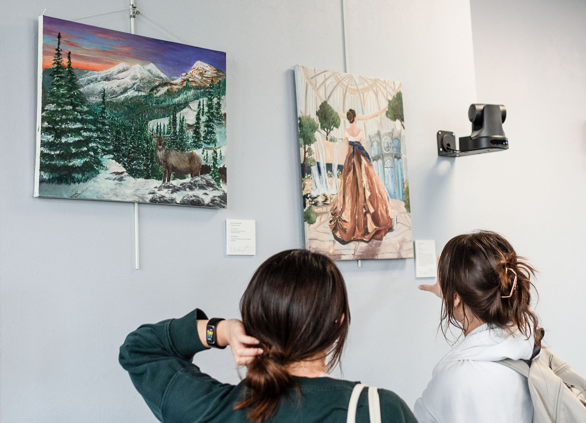 Students browse a pair of art pieces on the wall in the library. 