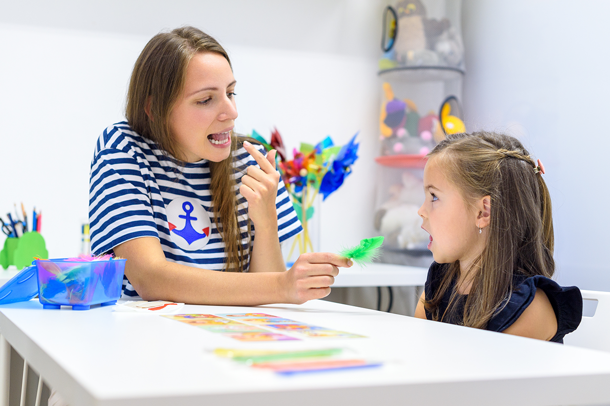 A speech therapist works with a preschool girl in the formation of sounds by demonstrating articulation with her tongue