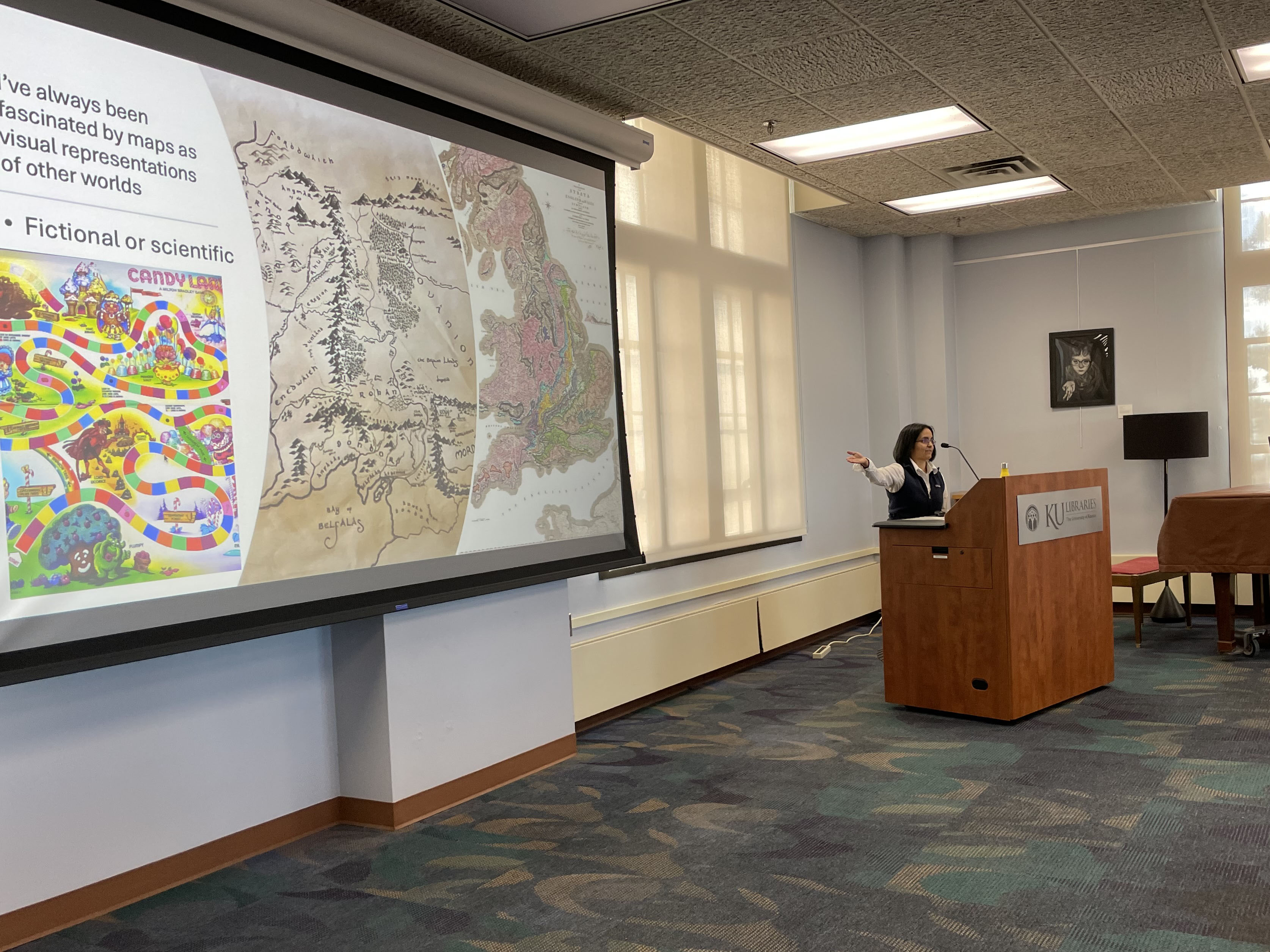 woman presents from podium, gesturing toward screen