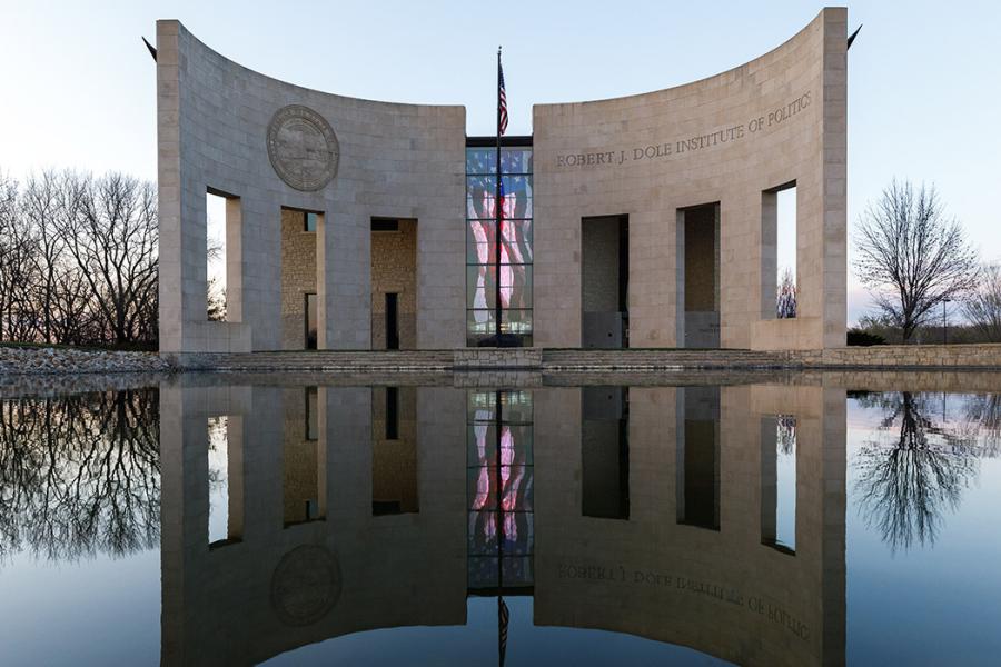 Dole Institute of Politics, shown in reflecting pool on fall day. Trees with bare branches.