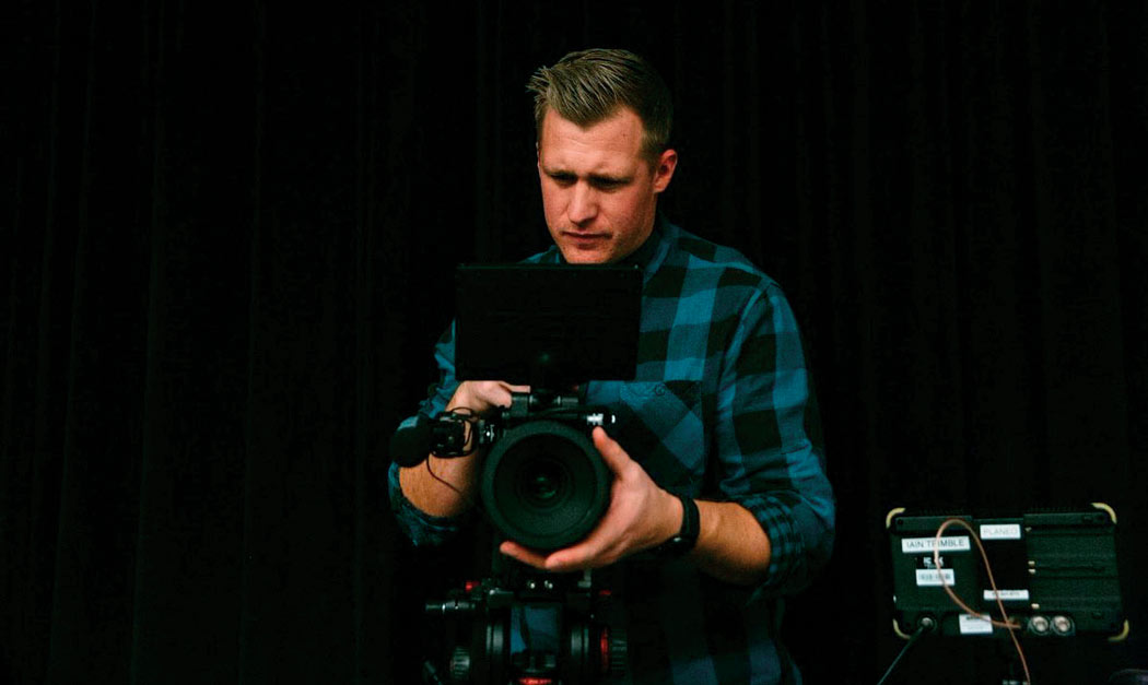 A man looks through a film camera against a dark background.