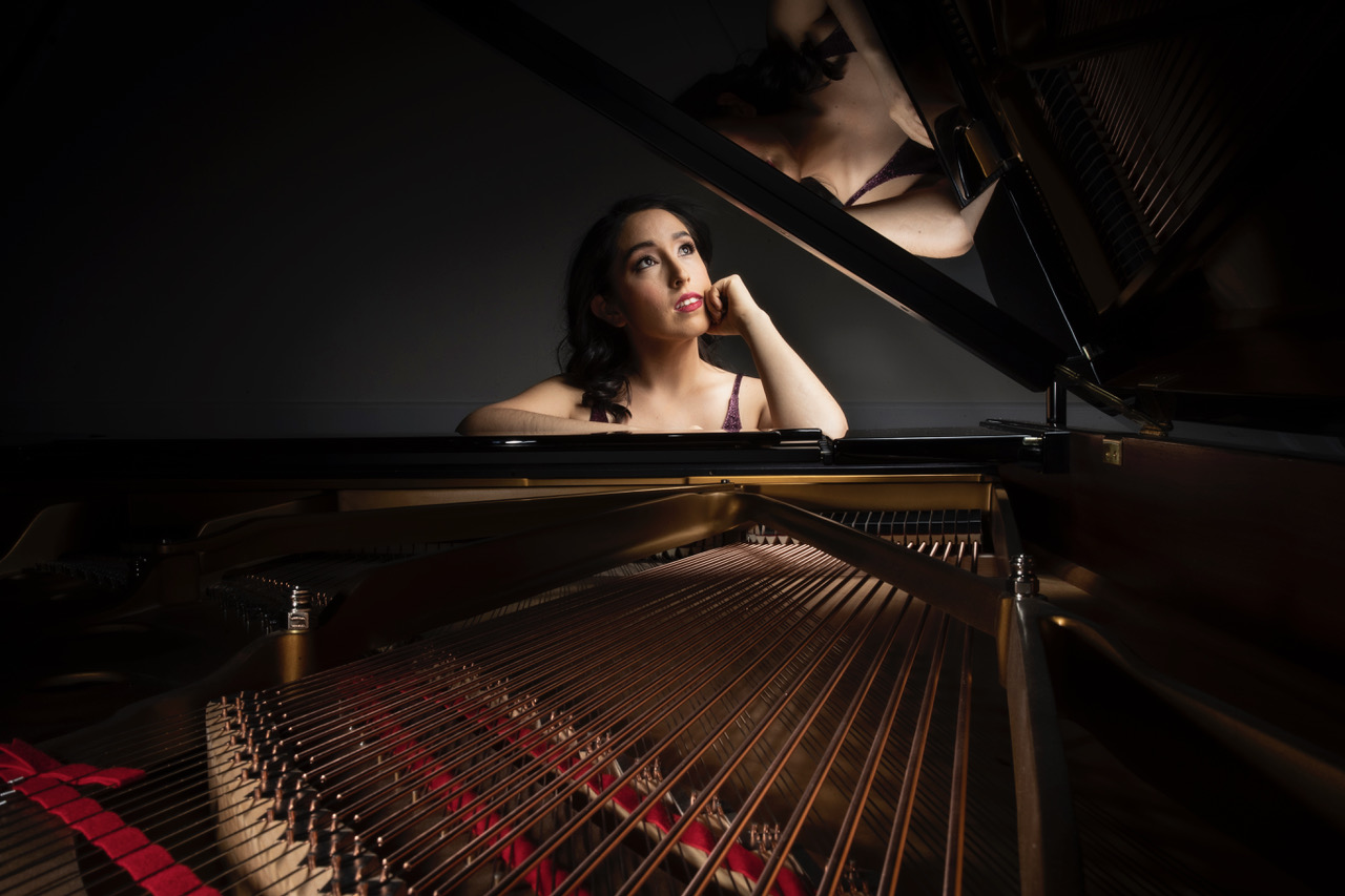 a woman seated behind a piano gazing upwards