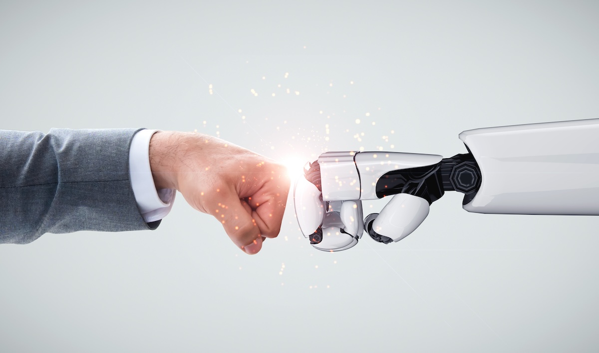 The arm of a businessman fist bumps the arm of a robot.