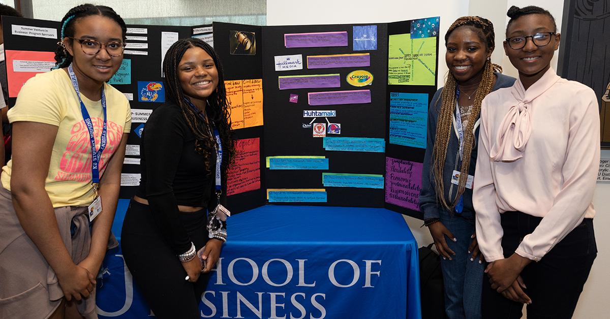 Four girls stand around a poster board that outlines their experience during the 2023 Summer Venture in Business.