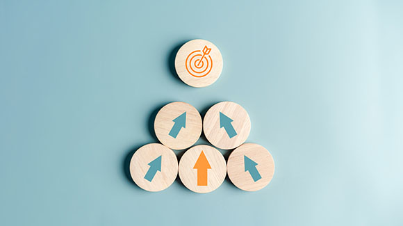 Wooden buttons decorated with arrows pointing toward top button with bull's-eye on blue background. Adobe stock image.