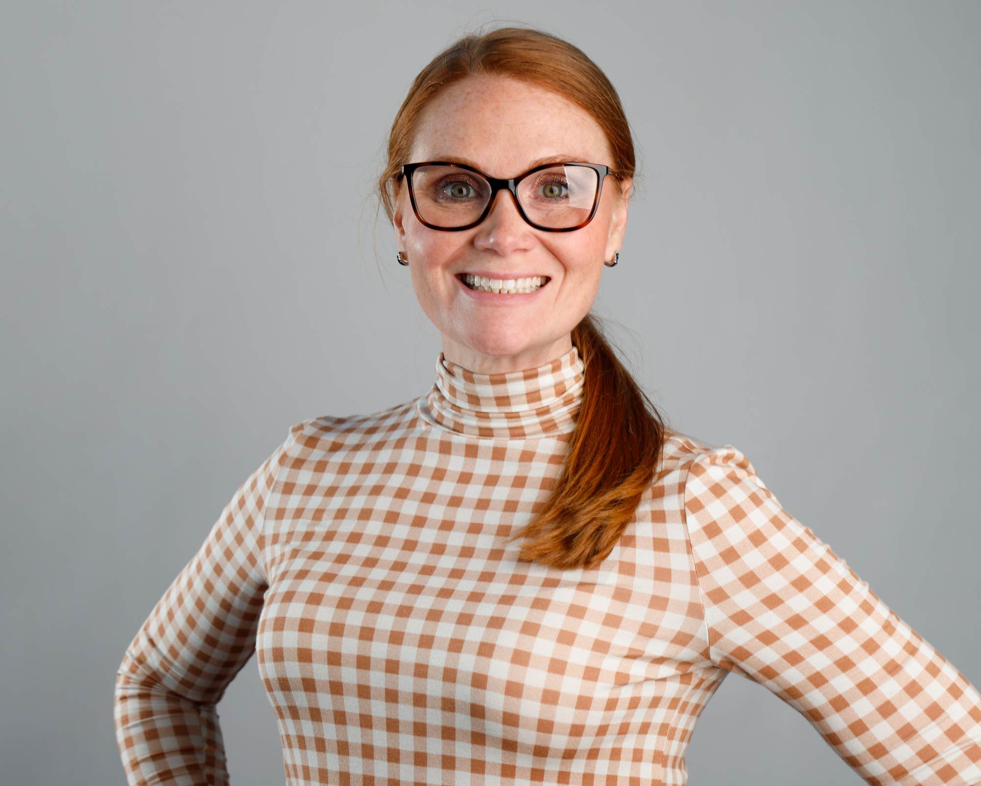 A photo of Kari Murphy wearing glasses, a checkered shirt, and small hoop earrings.