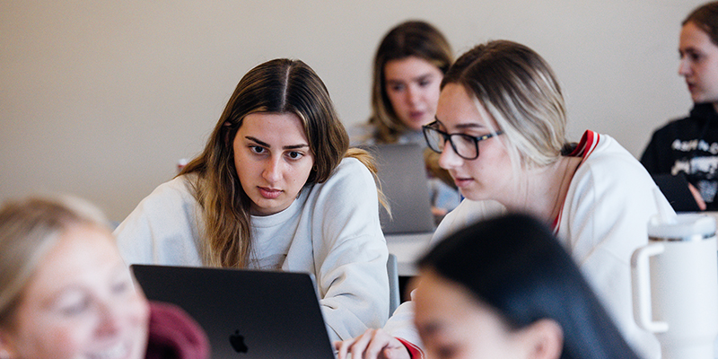 Group of students concentrated on working together with laptops, in a classroom setting.