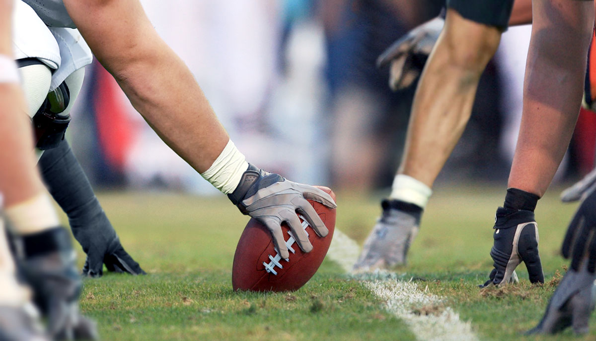 An image of football players' hands touching the ground as they line up for a play.